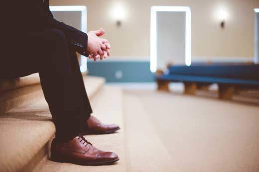 Side view of a man sitting on church sanctuary steps, hands folded, contemplating why do SDA worship on Saturday.