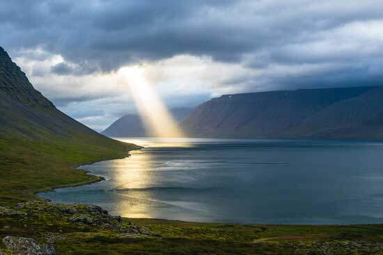 Sunlight piercing through the dark clouds on the sea, surrounded by mountains, reminding us of God's love & care