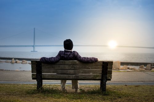 A person sitting on a bench at seashore looking at sunset at the horizon, as we discover blessings of Sabbath for ourselves.