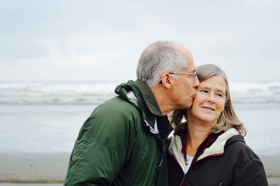 A gray-haired man kissing his wife on a beach and enjoying a quality life because of good health habits and trust in God