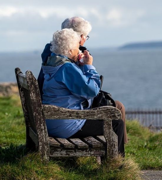 An elderly couple sitting outdoors by a lake as they enjoy the long life resulting from their healthy lifestyle