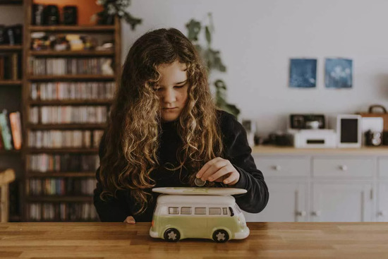 Girl putting a coin into a piggy bank to be a good steward of her money.