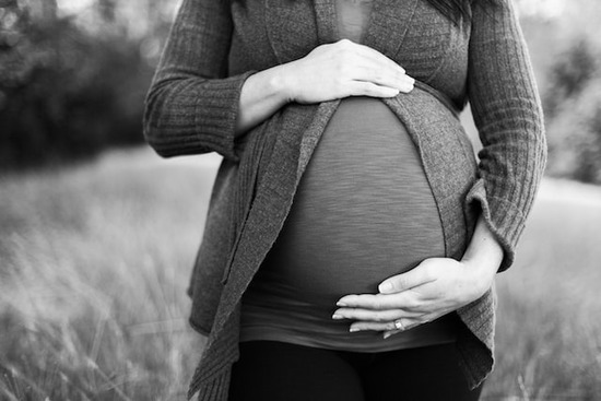 A pregnant woman with her hand on her belly, praying for her growing child