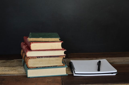 A stack of books, notebook, and a pen for Bible study