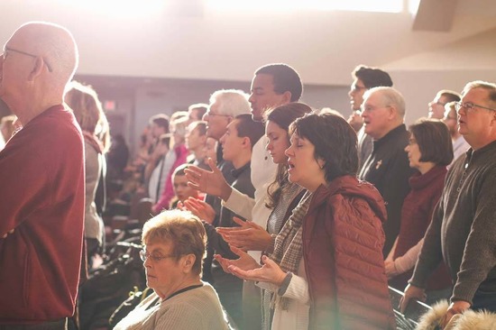 Church Congregation standing from their pews & singing Amen during worship with closed eyes and open hands